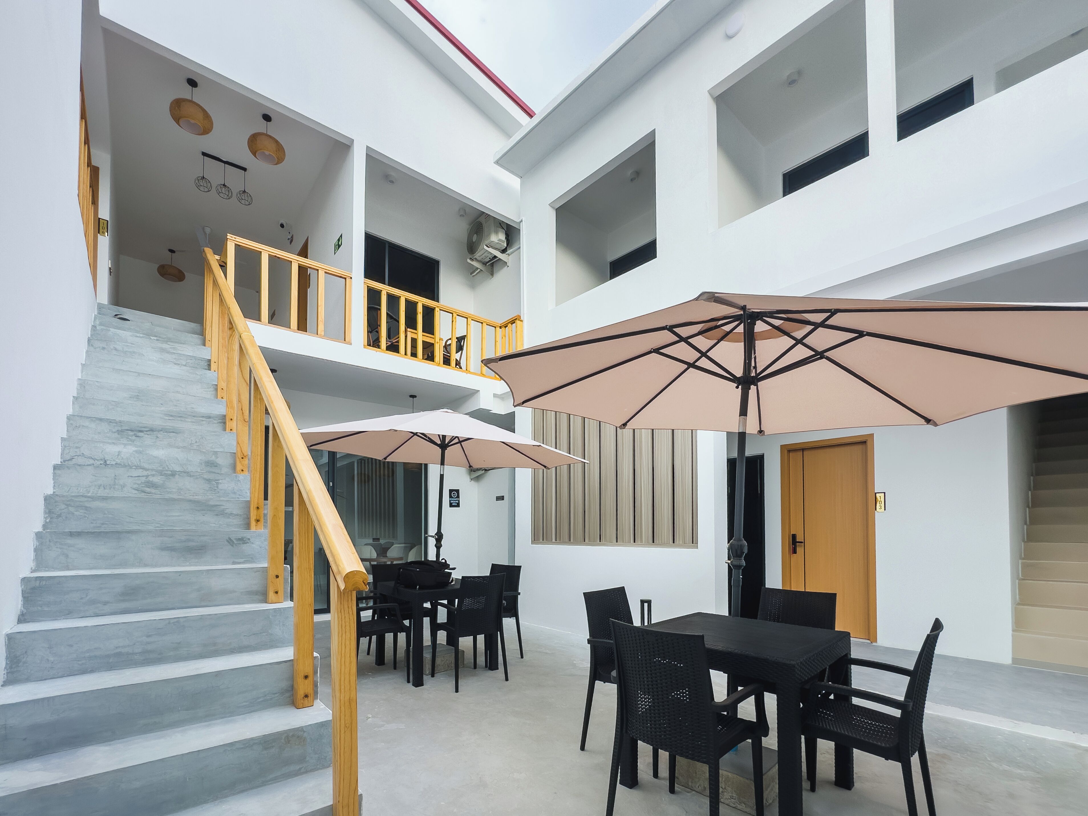 Un interior de varios niveles con escalera, comedor y zona de estar exterior con sombrillas.