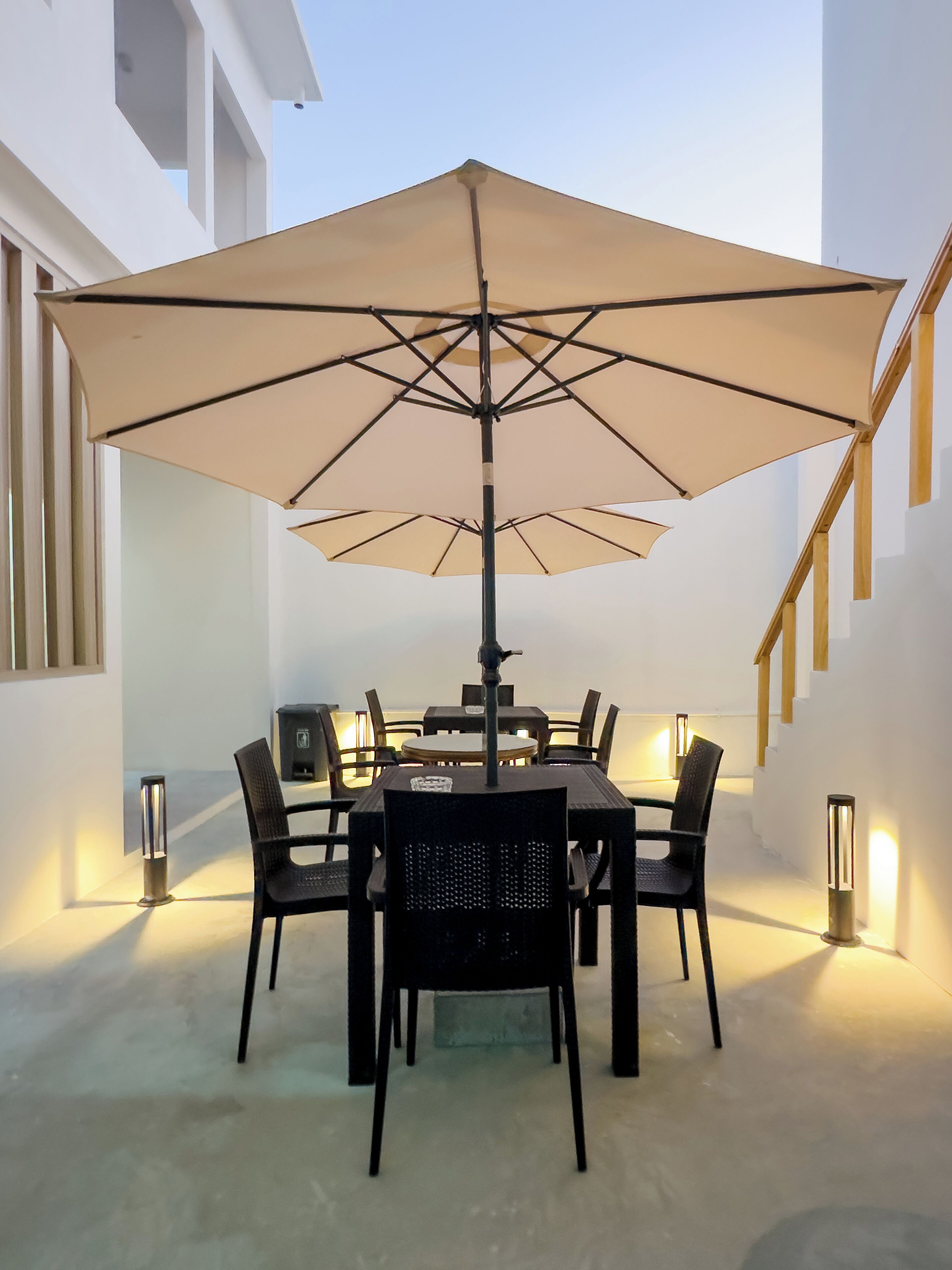 Un comedor con una mesa, sillas, un paraguas y luces fijadas a la pared.