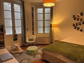 A bedroom with a bed, a desk with a laptop, a chair, a radiator, and a wall with photos. - Large, quiet family home with jacuzzi in the heart of Cognac (Cognac)