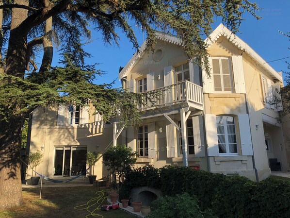 A two-story building with a balcony, a covered porch, and a small garden area with potted plants. - Large, quiet family home with jacuzzi in the heart of Cognac (Cognac)