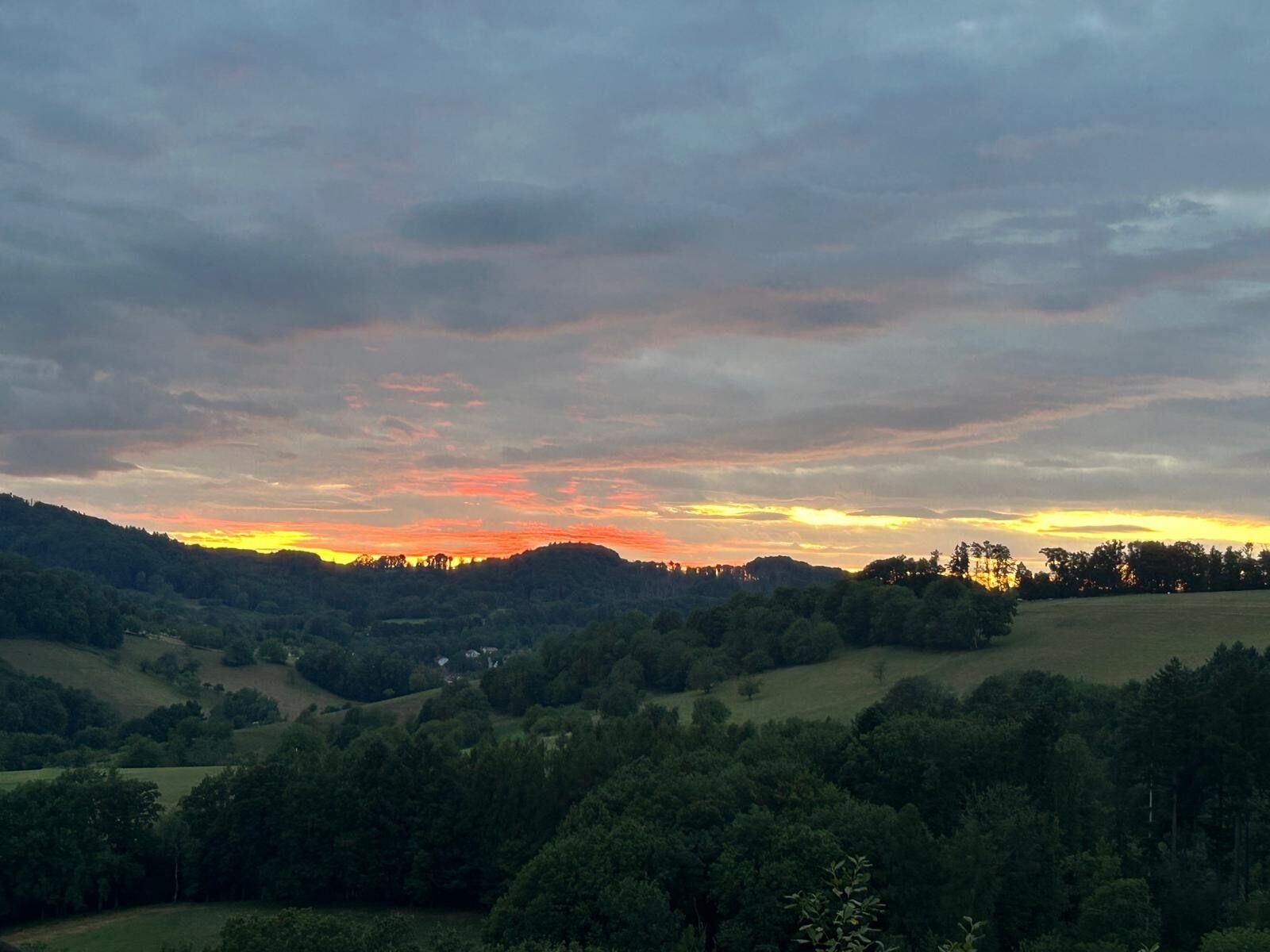 A landscape with rolling hills, trees, and a sunset.