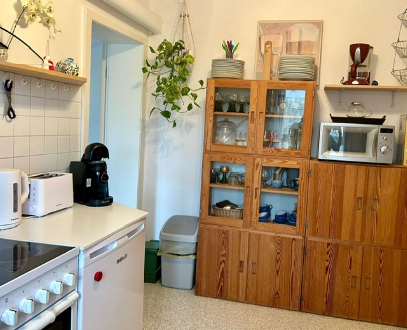 Et kompakt køkken med brødrister, kaffemaskine, mikrobølgeovn og træskabe.