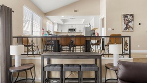 A spacious living area with a dining table, chairs, and a kitchen in the background. - Pool • Hot tub • Arcades • Air Hockey • Foosball • Mini-Golf • 20 Guests (Las Vegas)