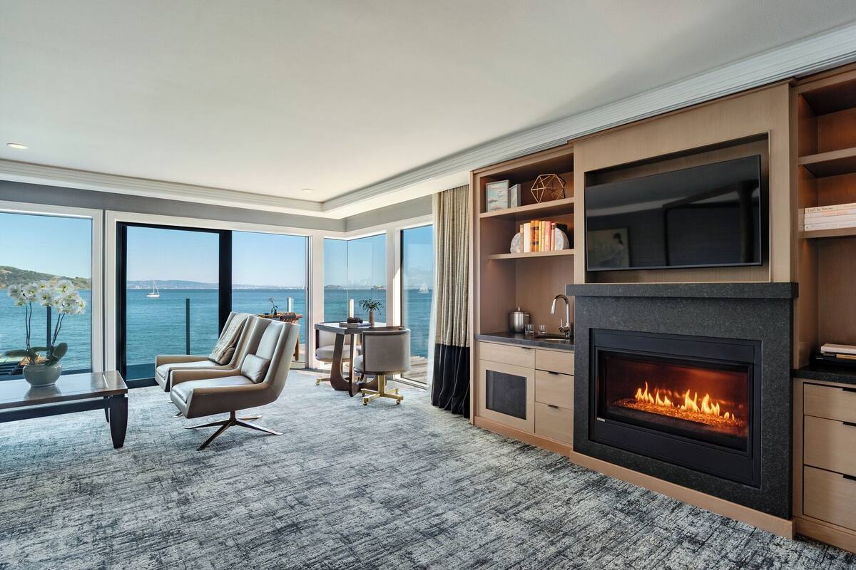 Una sala de estar moderna con chimenea, ventanas amplias y vista al mar.