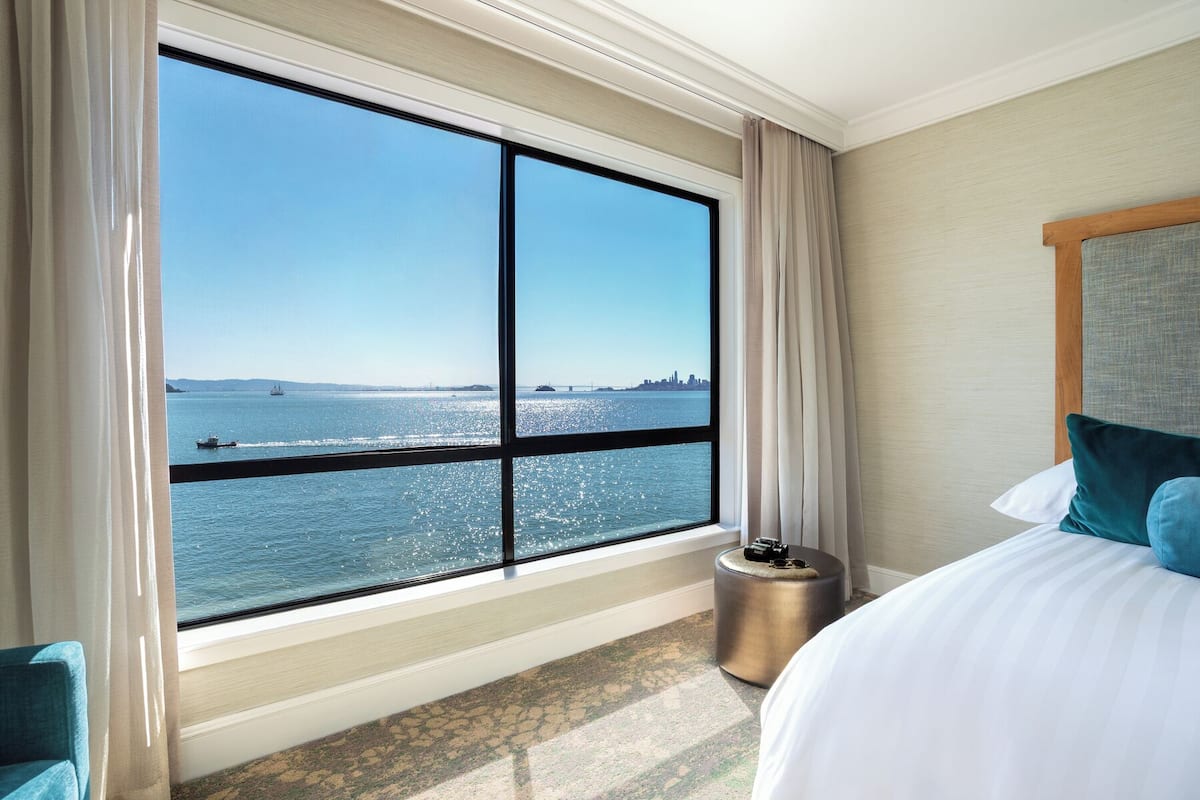 Habitación de hotel con un ventanal que ofrece vistas al agua y al horizonte lejano de la ciudad.