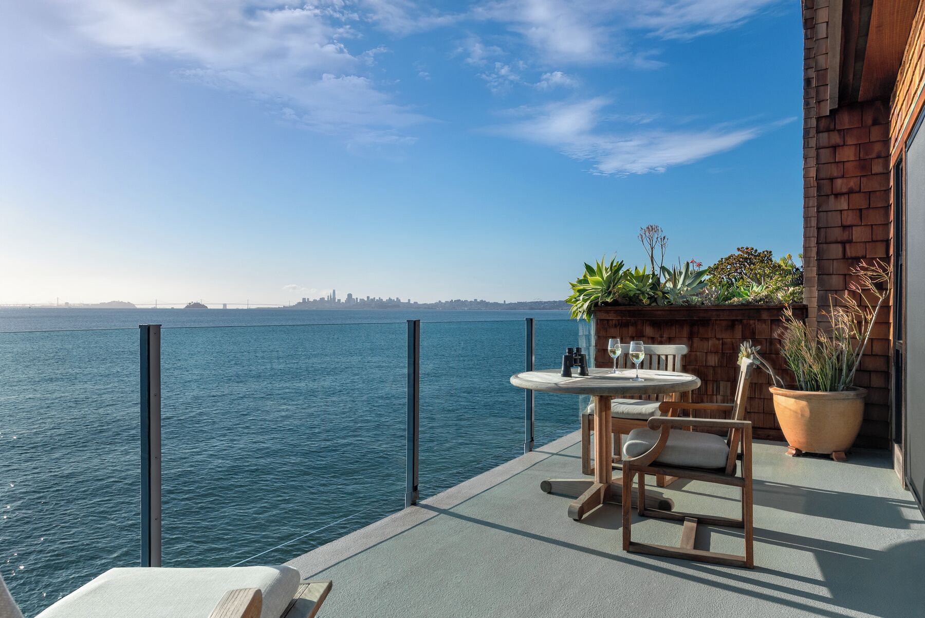 Een balkon met uitzicht op het water, een tafel met stoelen en bloempotten.
