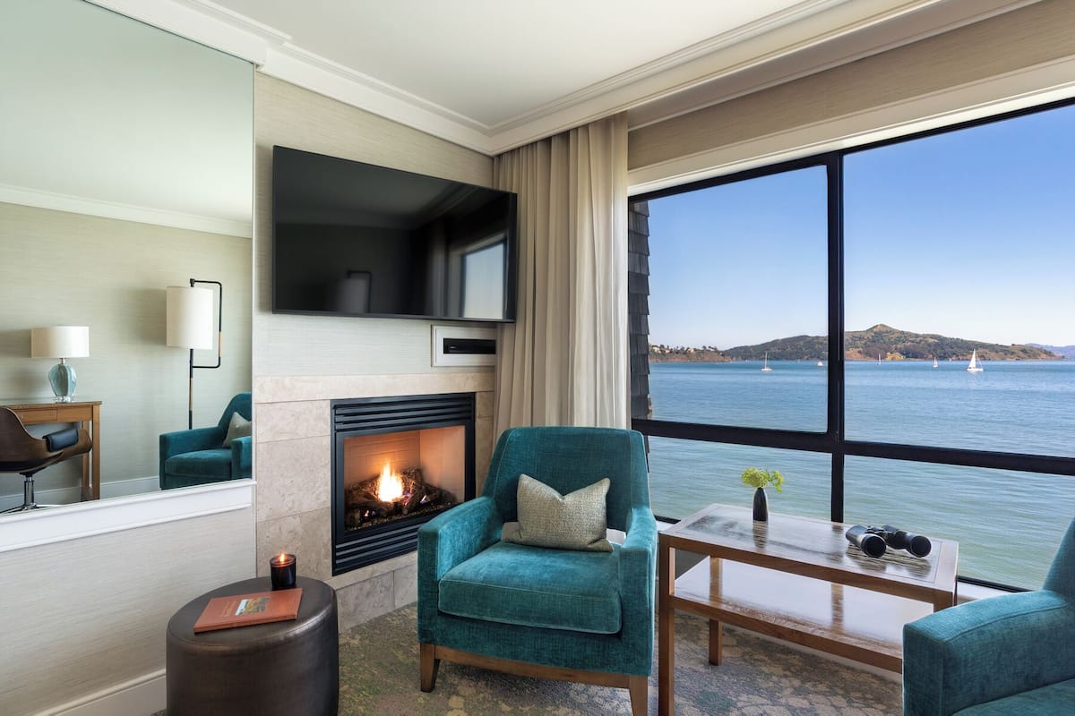 Un salón con chimenea, televisor, un ventanal con vistas al mar y una mesa con prismáticos.