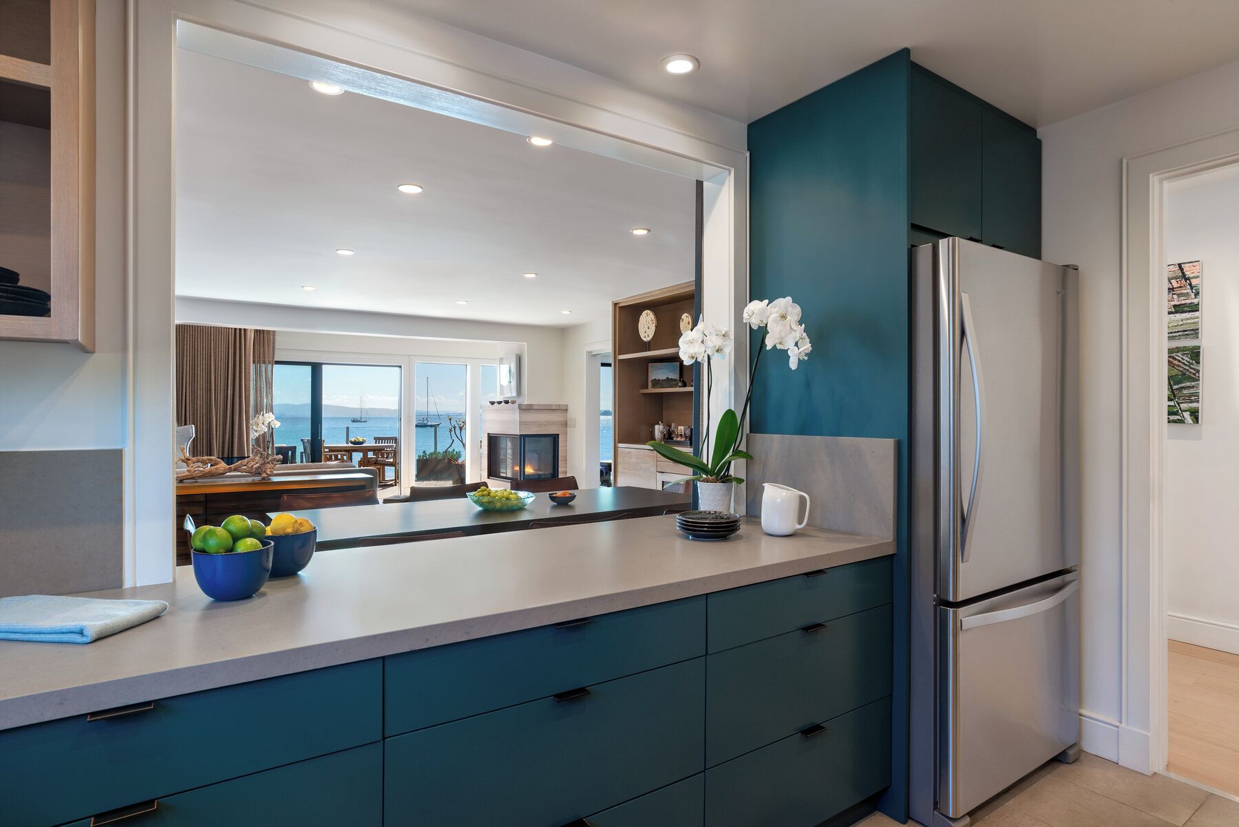 A modern kitchen with a large island, a refrigerator, and a view of the sea.