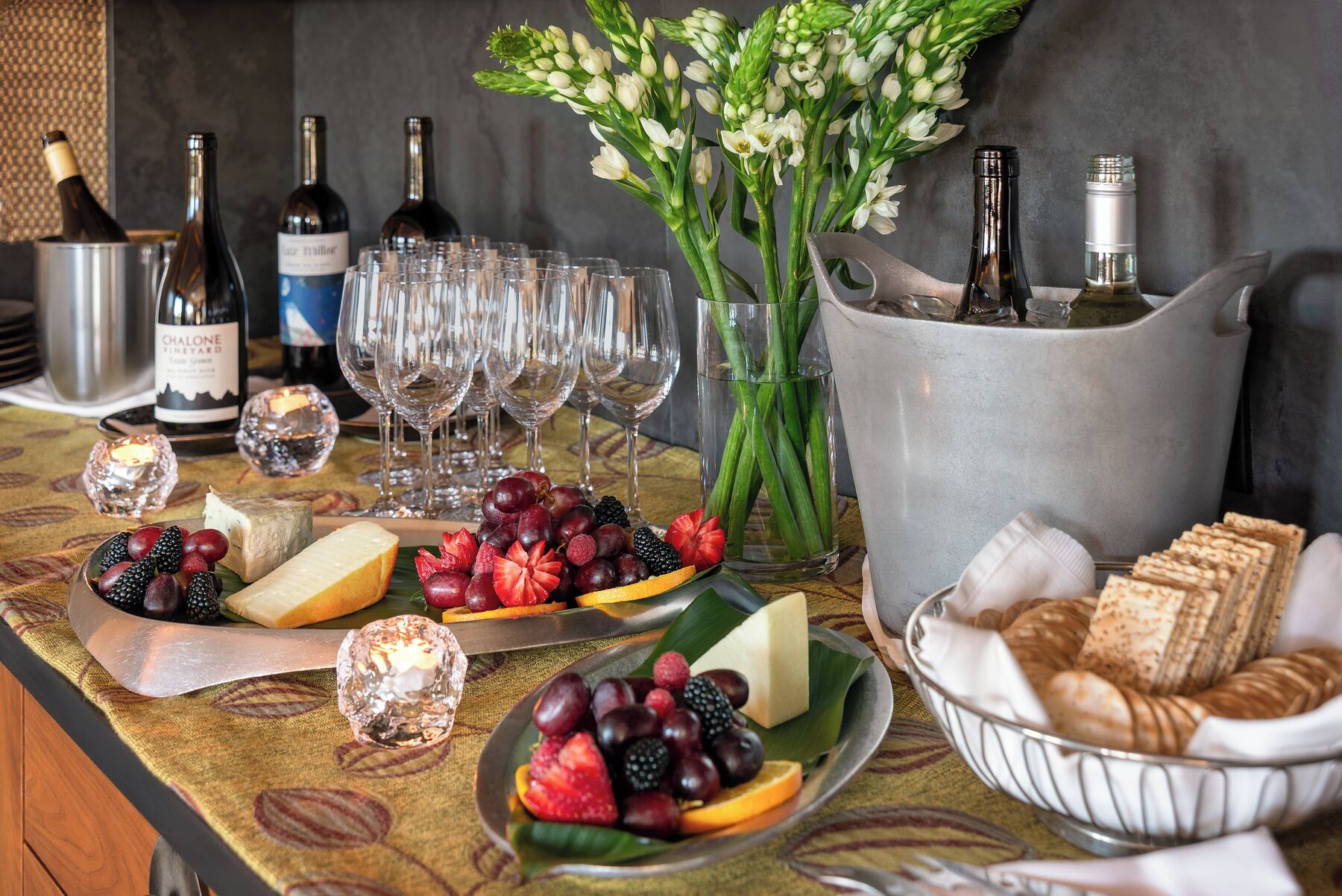 A table with wine bottles, glasses, cheese, fruits, and bread.
