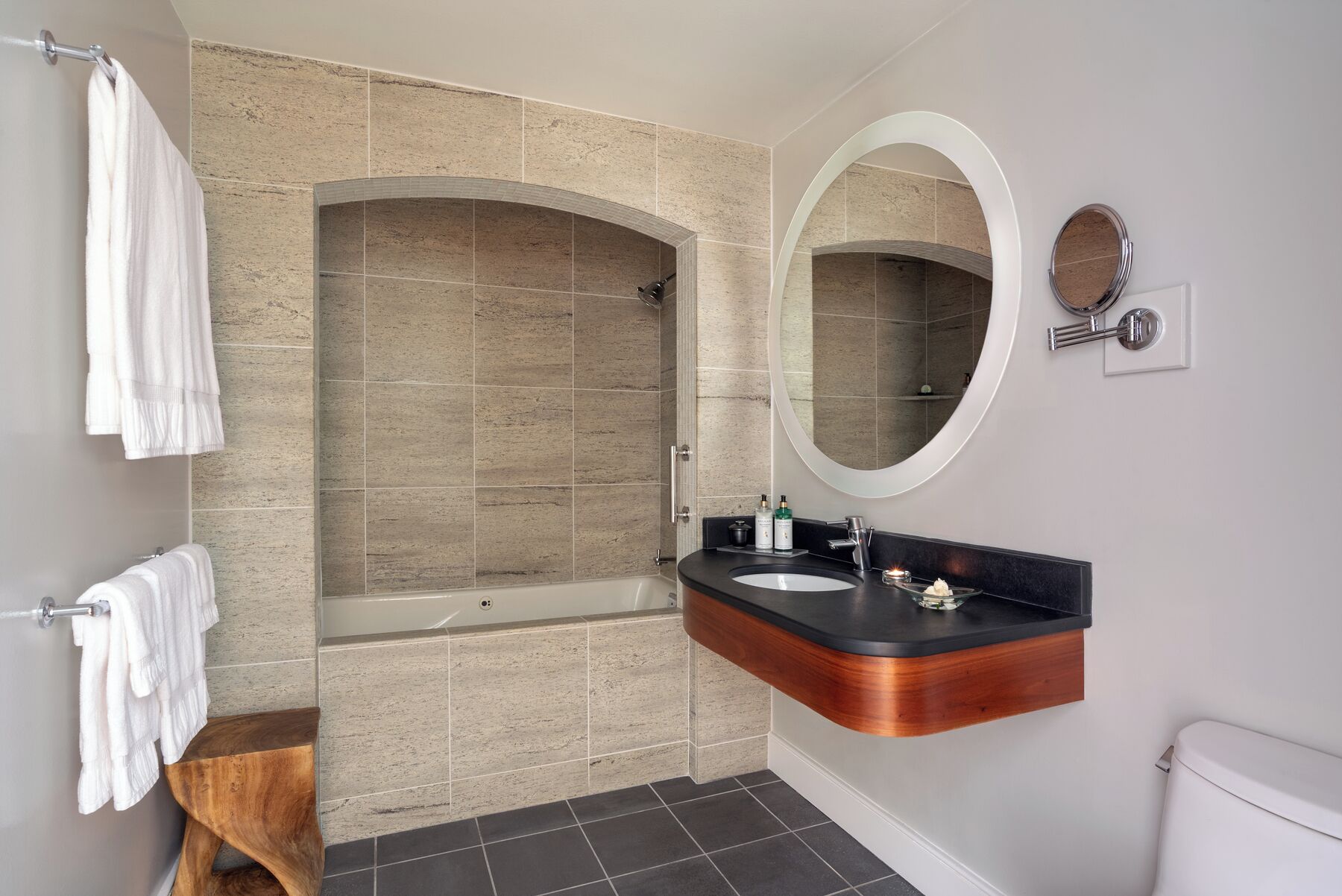 A modern bathroom with a freestanding bathtub, a vanity with a black countertop, and a wall-mounted mirror.
