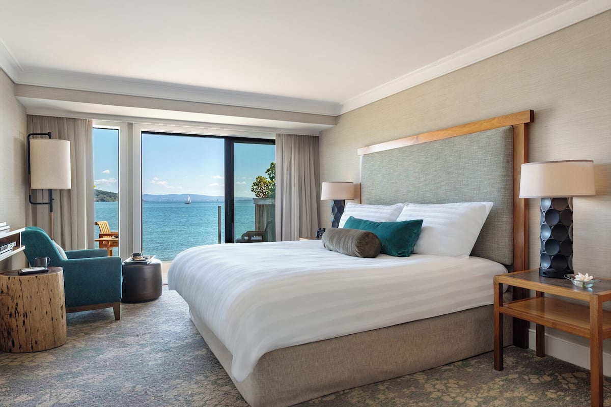 Habitación de hotel con una cama grande, dos mesitas de noche, un escritorio, una silla y vistas al mar.