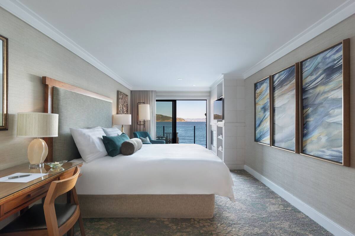 Una habitación de hotel con una cama grande, un escritorio, una silla, un televisor y vistas al mar.