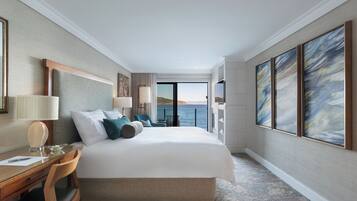 A hotel room with a large bed, a desk, a chair, a TV, and a view of the sea.