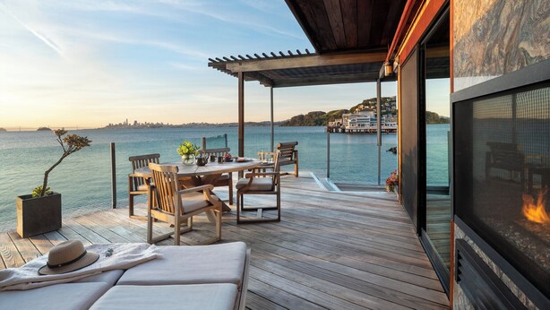 Un patio in legno con tavolo e sedie, un divano, un caminetto e vista sull'acqua e sullo skyline della città.