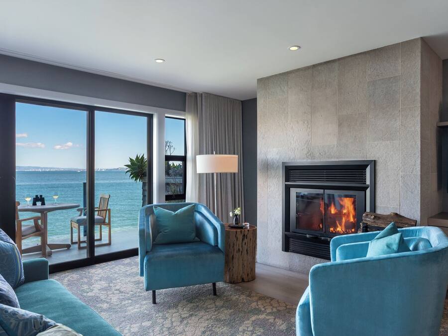 A modern living room with a fireplace, large windows overlooking the sea, and a cozy seating area.