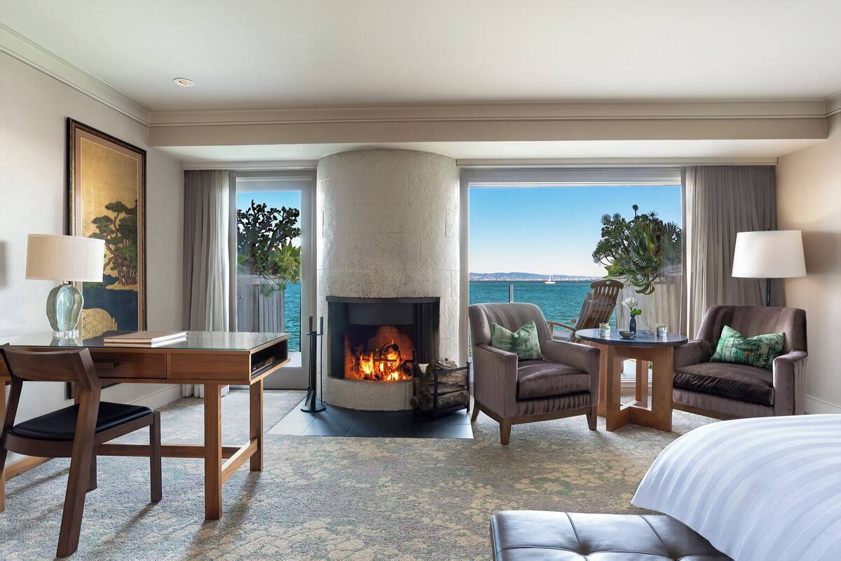 Una habitación de hotel con chimenea, escritorio, dos sillones, sofá y cama.