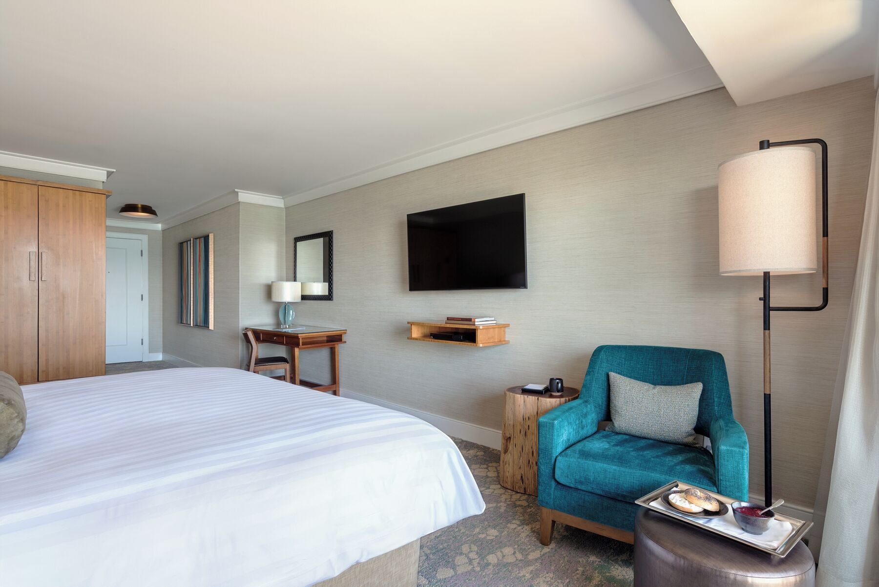 A hotel room with a bed, a desk, a chair, a TV, and a lamp.