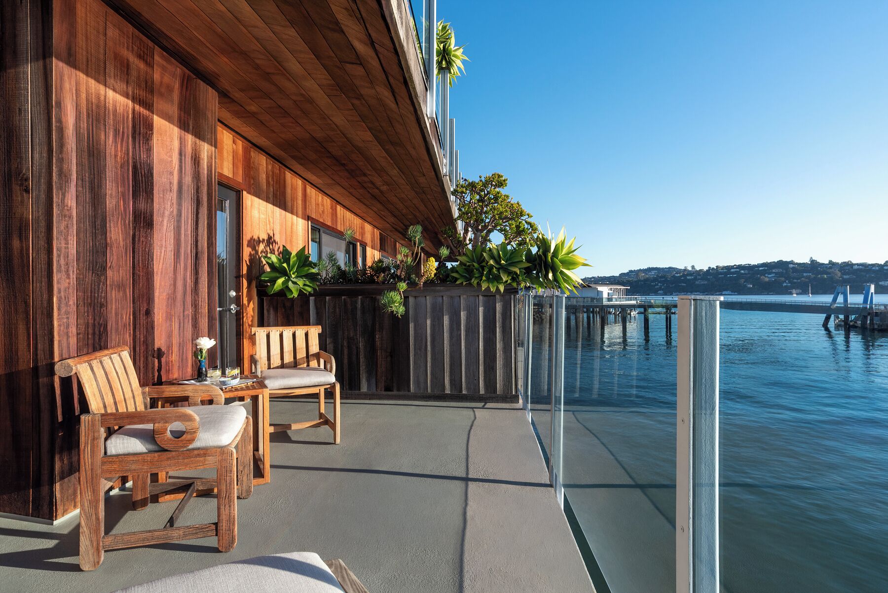 A wooden exterior wall, outdoor seating, a glass railing, and a view of the water.