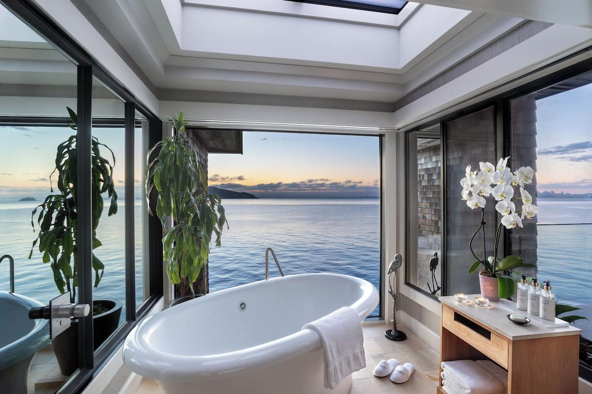 Un baño moderno con una bañera independiente, un tocador y un amplio ventanal con vistas al mar.