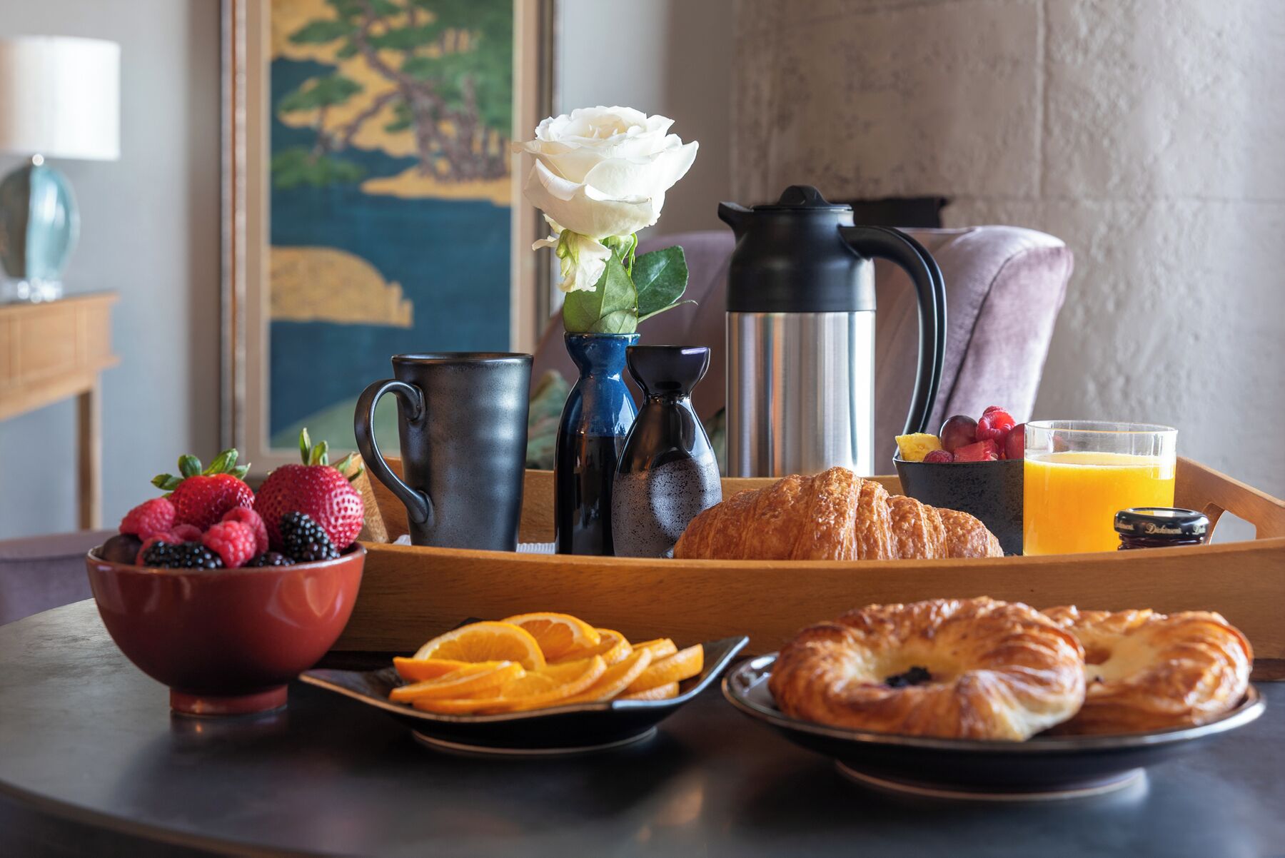 A breakfast tray with fruits, pastries, a coffee pot, and a thermos.