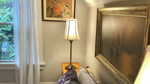Et soveværelse med seng, et natbord, en lampe, et maleri og et vindue med gardiner.