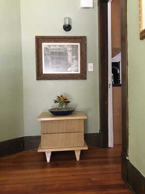 A hallway with a framed picture on the wall, a small table with a vase of flowers, and a light fixture above the table. - Cleveland Clinic, 7 minutes from: Oak3 (Cleveland Heights)