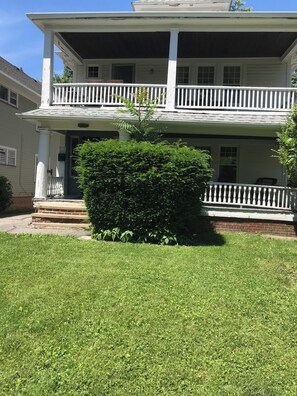 A two-story house with a porch, a well-maintained lawn, and a small hedge. - Cleveland Clinic, 7 minutes from: Oak3 (Cleveland Heights)