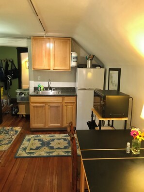 A compact kitchen with wooden cabinets, a refrigerator, a microwave, and a dining table with a vase of flowers. - Cleveland Clinic, 7 minutes from: Oak3 (Cleveland Heights)