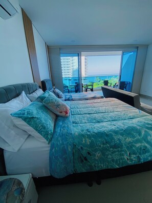 Ein Hotelzimmer mit einem großen Bett, einem Schreibtisch und einem Balkon mit Blick auf Gebäude und Grünflächen.
