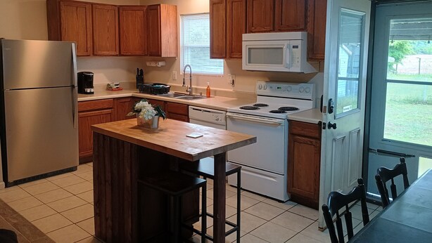 A kitchen with wooden cabinets, a stainless steel refrigerator, a microwave, a stove, and a sink.