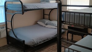 A bunk bed room with a ceiling light fixture, a window with blinds, and a heater on the wall.