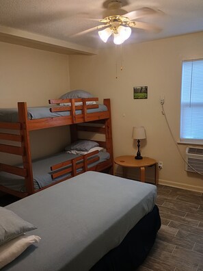 A room with bunk beds, a round table with a lamp, an air conditioning unit, and a ceiling fan.