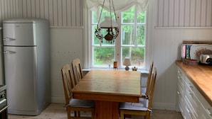 Una cocina con una mesa de madera, sillas, un refrigerador y una ventana con cortinas.