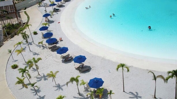 Ein Strand mit weißem Sand, Palmen und blauen Sonnenschirmen.