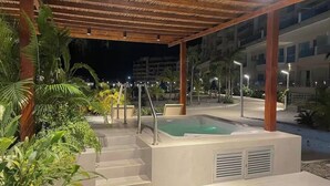 Ein überdachter Außenbereich mit einem Whirlpool, Treppen und umgebender Bepflanzung.