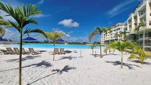 Ein Strand mit Liegestühlen, einem Pool und Palmen.