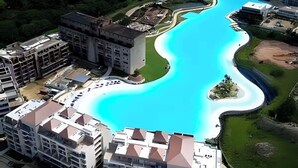 Ein großer Hotelkomplex mit einem zentralen Schwimmbecken, mehreren Gebäuden und umliegender Grünfläche.