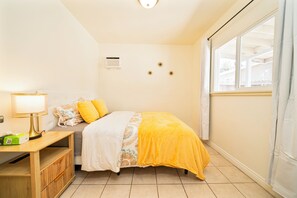 Une chambre à coucher comprenant un lit, un bureau, une lampe, une fenêtre et un climatiseur fixé au mur.