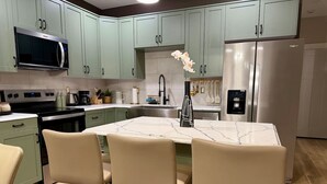 Una cocina moderna con armarios verde claro, encimera de mármol y refrigerador de acero inoxidable.