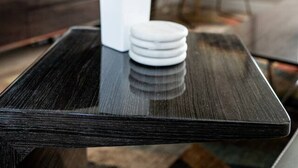 Una sala de estar moderna con una mesa de centro de madera oscura, un jarrón blanco con una planta y una pila de platos blancos.