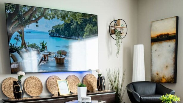 Una sala de estar moderna con un televisor de pantalla plana grande, un sofá blanco, un sillón de cuero negro, una mesa de centro de madera y un adorno de pared.