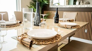 Una mesa de comedor dispuesta con platos, vasos y una botella de vino, con un espejo y plantas al fondo.
