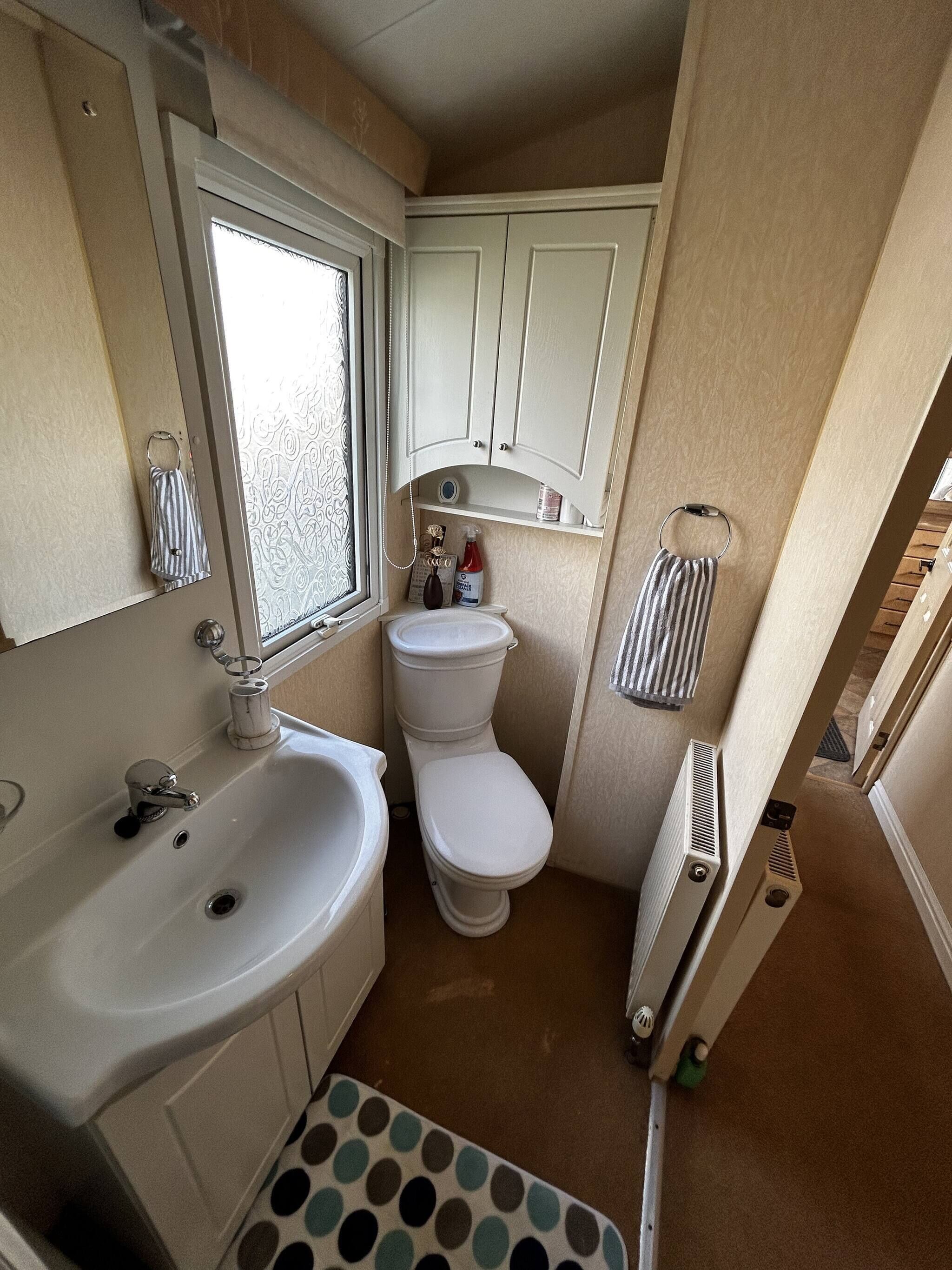 Een kleine badkamer met een wastafel, toilet en raam.