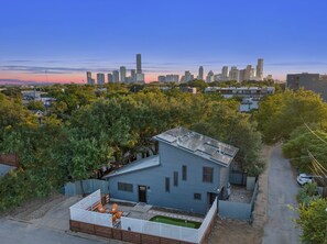 Zona residencial con una casa azul que cuenta con un pequeño patio y vistas a un horizonte urbano de fondo.
