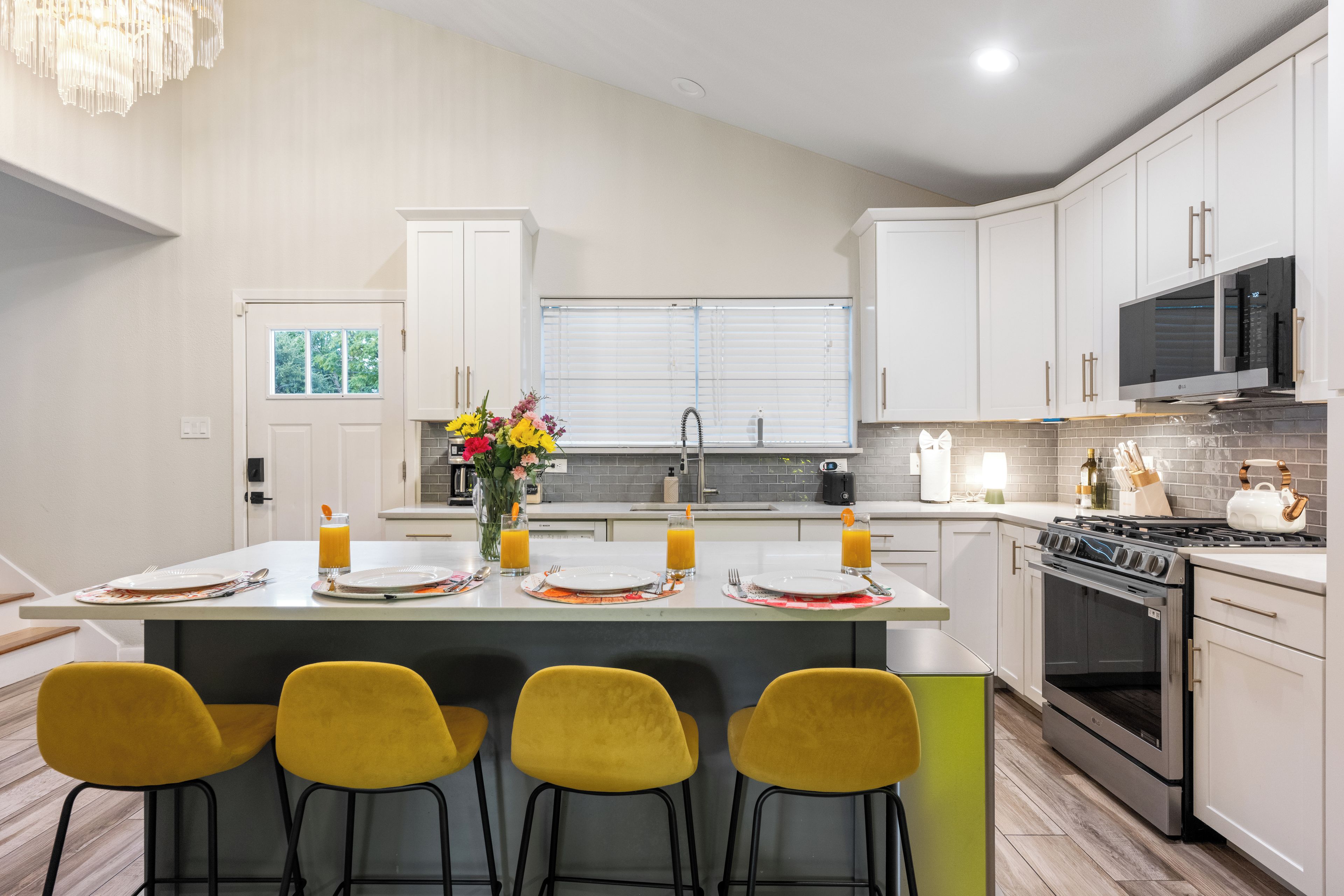 A modern kitchen with white cabinets, a central island with bar stools, a stove, and a microwave.