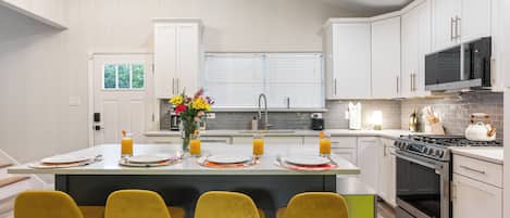 A modern kitchen with white cabinets, a central island with bar stools, a stove, and a microwave.