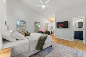 Ein Schlafzimmer mit einem Bett, einem Fernseher, einem Deckenventilator und einem Badezimmer mit Spiegel und Waschbecken.