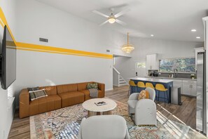 Ein modernes Wohnzimmer mit einer Couch, Sesseln, einem Couchtisch und einer Küchenzeile mit Bar.