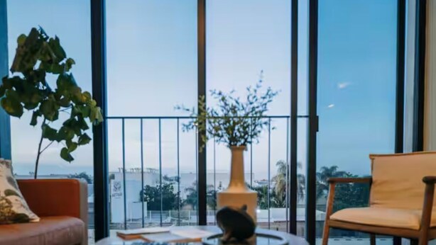 Ein modernes Wohnzimmer mit einer Couch, zwei Couchtischen, einer Topfpflanze und Blick durch große Fenster.