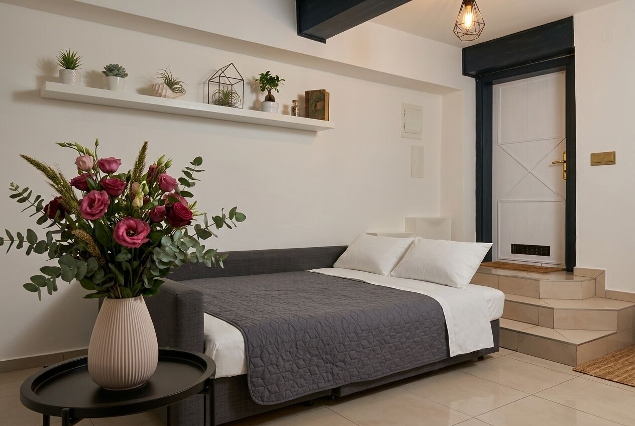 A bedroom with a bed, a bedside table with a vase of flowers, a shelf with plants, and a door with a cross design.